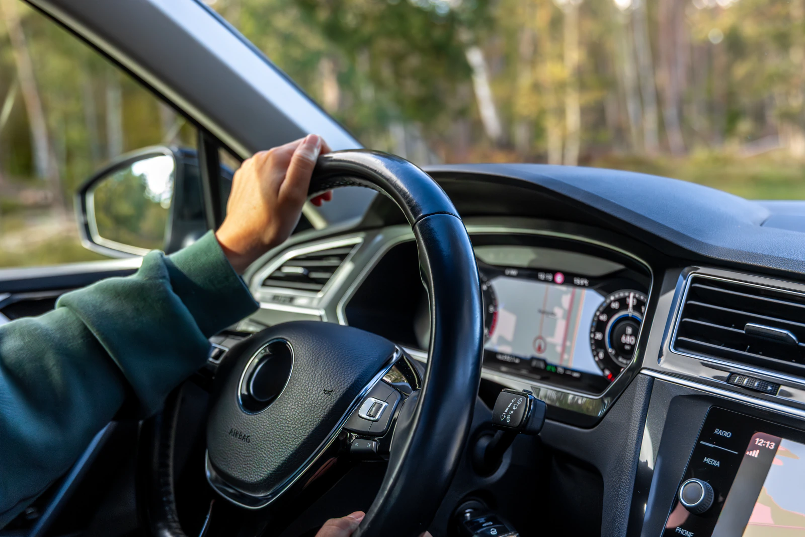Hand am Lenkrad bei einer Autofahrt durch den Wald